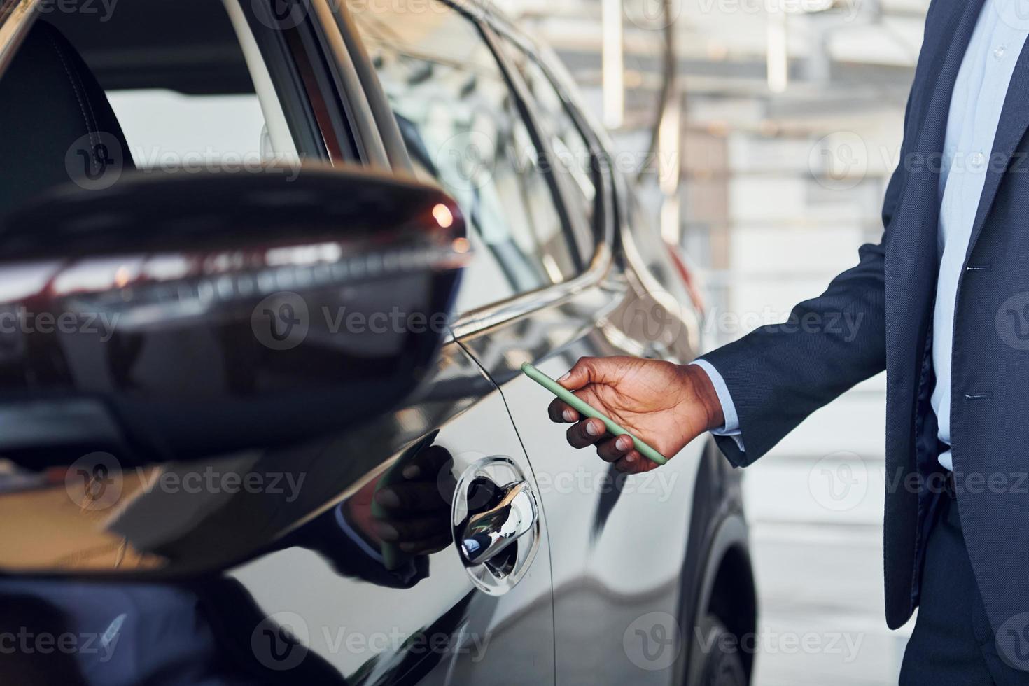 usando smartphone para abrir a porta. jovem empresário afro-americano em terno preto é o autosalon foto