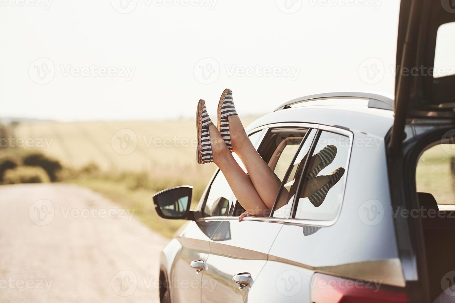 em chinelos listrados preto e branco. menina põe as pernas para fora na janela do automóvel na zona rural foto
