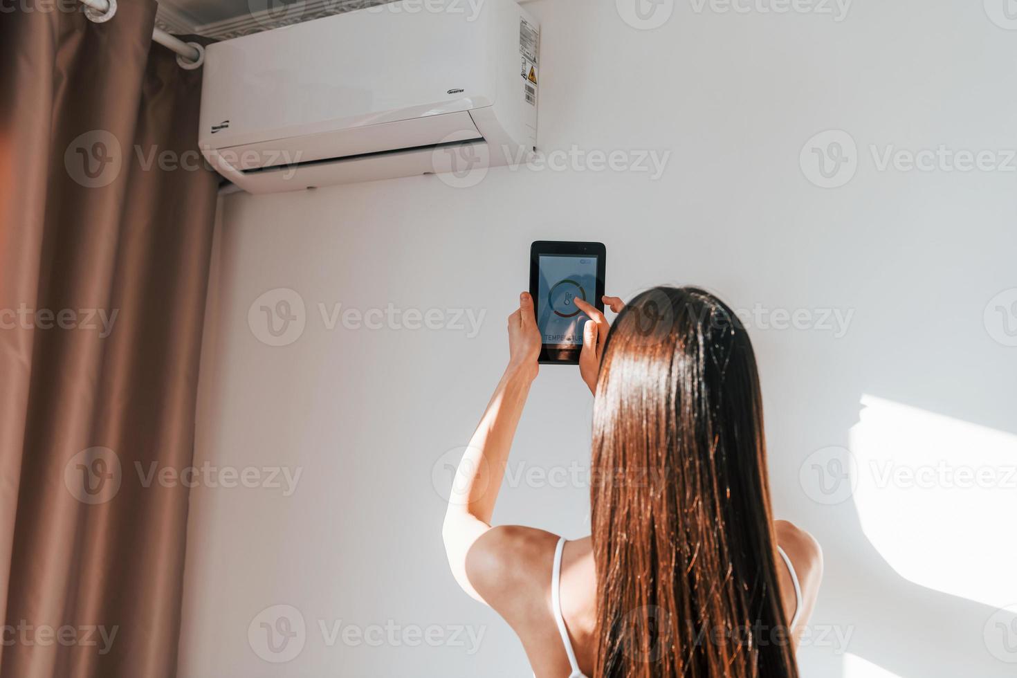 vista traseira da mulher que está dentro de casa com telefone e controlando a tecnologia de casa inteligente foto