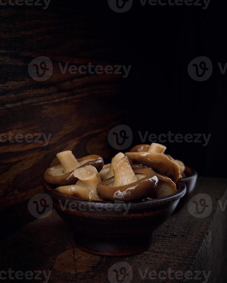 uma xícara de barro cheia de deliciosos cogumelos em conserva fica sobre uma mesa de madeira. comida rústica. foto