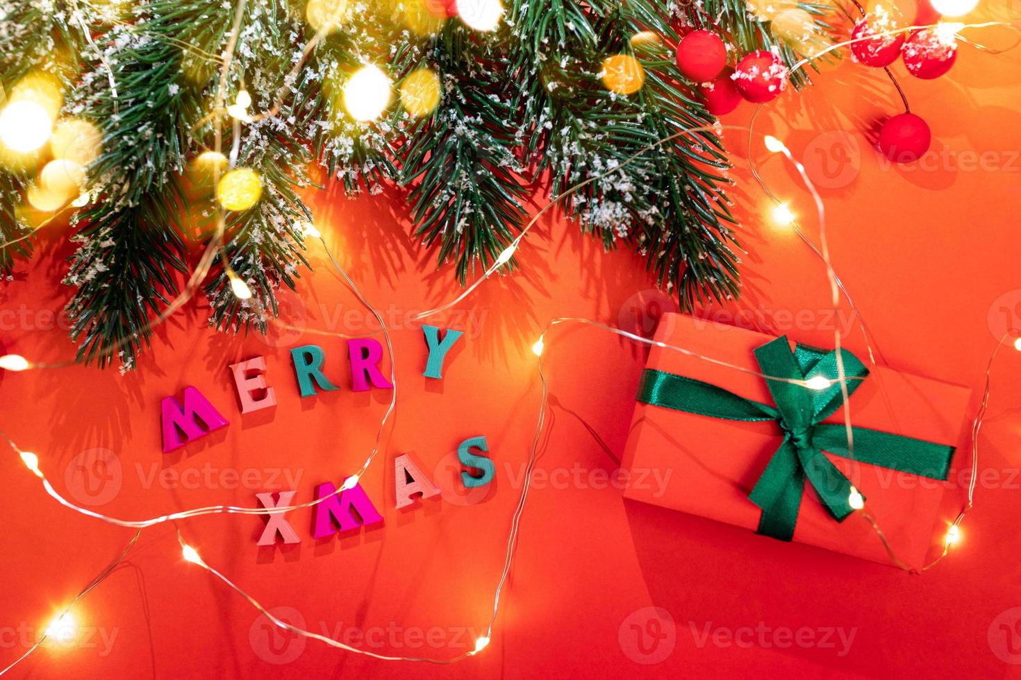 ramos de abeto, luzes de natal, neve, bagas vermelhas, letras coloridas feliz natal, caixa de presente diy, luzes de bokeh douradas em vermelho. foto