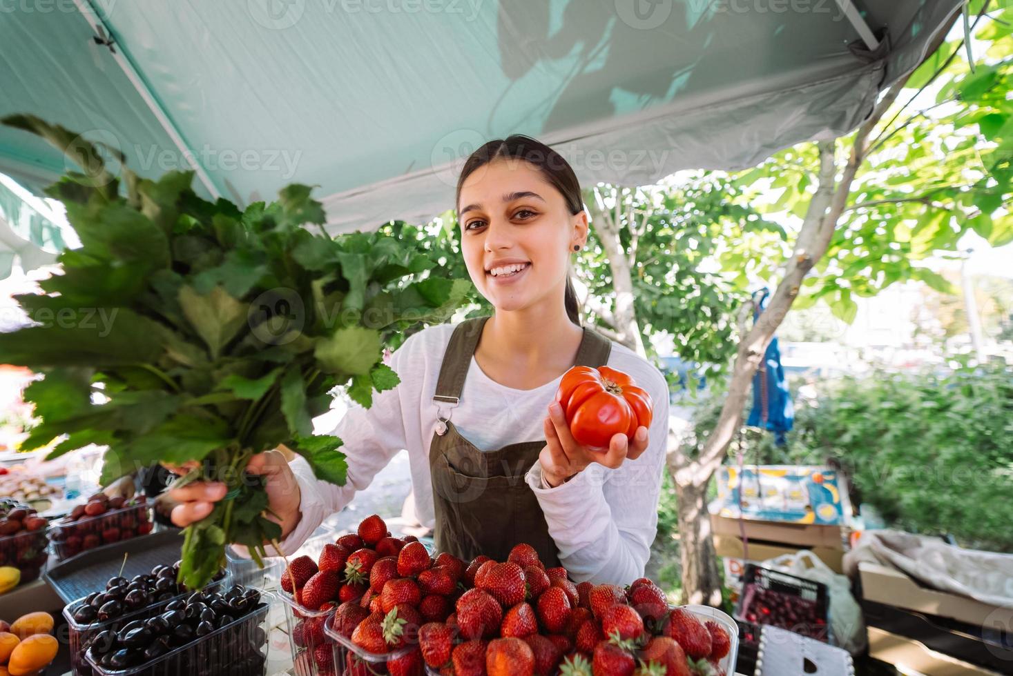 jovem vendedora no trabalho, segurando salsa e tomate nas mãos foto