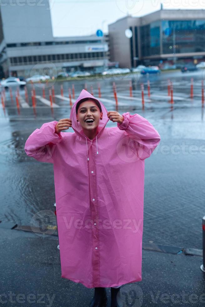 jovem sorridente em uma capa de chuva rosa, aproveitando um dia chuvoso. foto