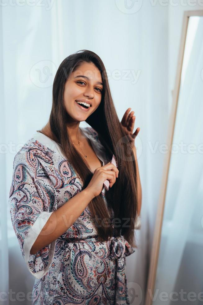 mulher jovem e bonita penteando o cabelo na frente do espelho. foto