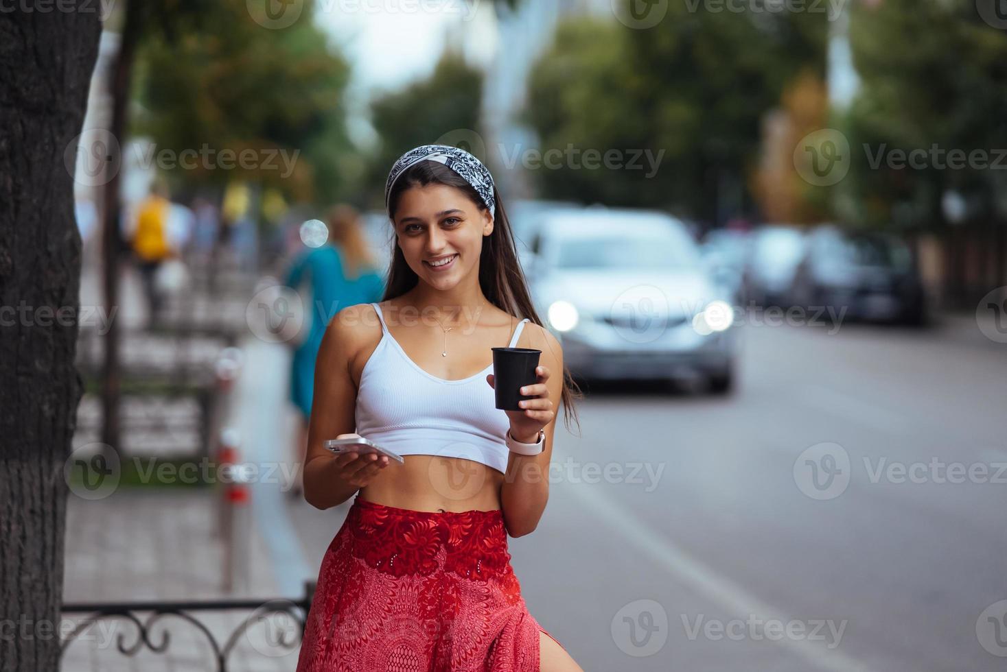 mulher na rua bebendo café da manhã e usa smartphone. foto