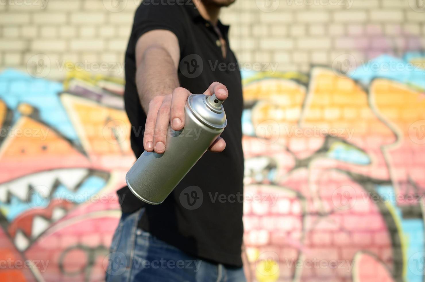 jovem grafiteiro aponta sua lata de spray no fundo do graffiti colorido em tons de rosa na parede de tijolos. arte de rua e processo de pintura contemporânea foto