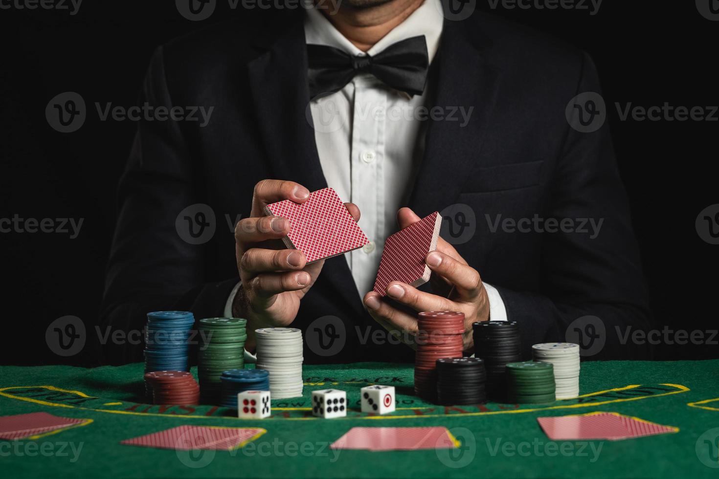 foto de corte de close-up homem dealer ou croupier embaralha cartas de pôquer apostando no cassino em fundo preto de mesa verde, negociante homem convite apostar cartas de baralho. cassino, pôquer, conceito de jogo de pôquer