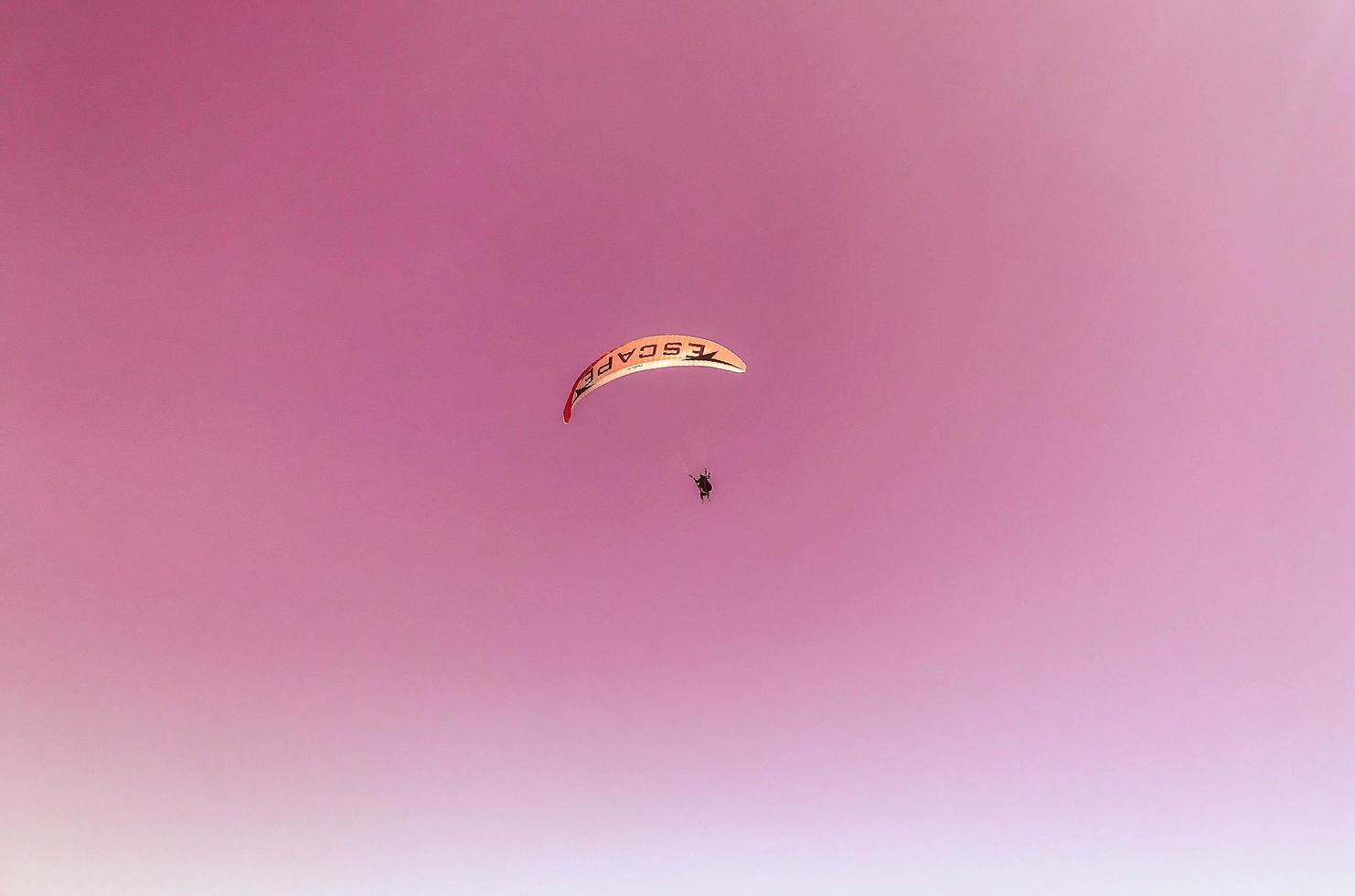 parapente em um país quente. pára-quedismo da montanha, recreação ativa. um homem em um traje de proteção está voando em um balão de ar quente em um céu rosa fofo foto