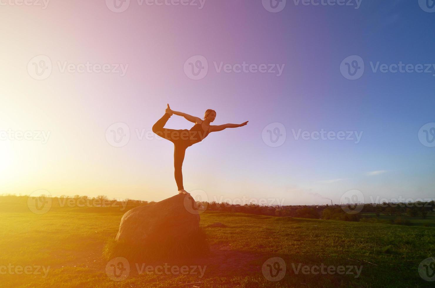 silhueta de jovem loira em traje esportivo pratica ioga em uma pitoresca colina verde à noite ao pôr do sol. o conceito de exercício e estilos de vida saudáveis foto