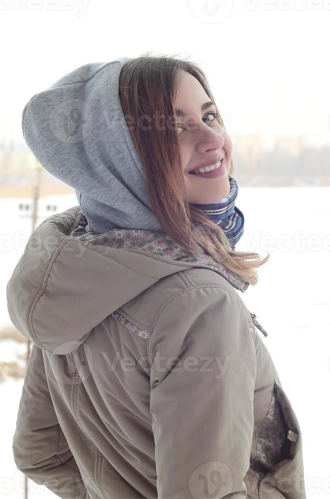 uma jovem e sorridente garota caucasiana olha ao redor da linha do horizonte entre o céu e o lago congelado no inverno foto