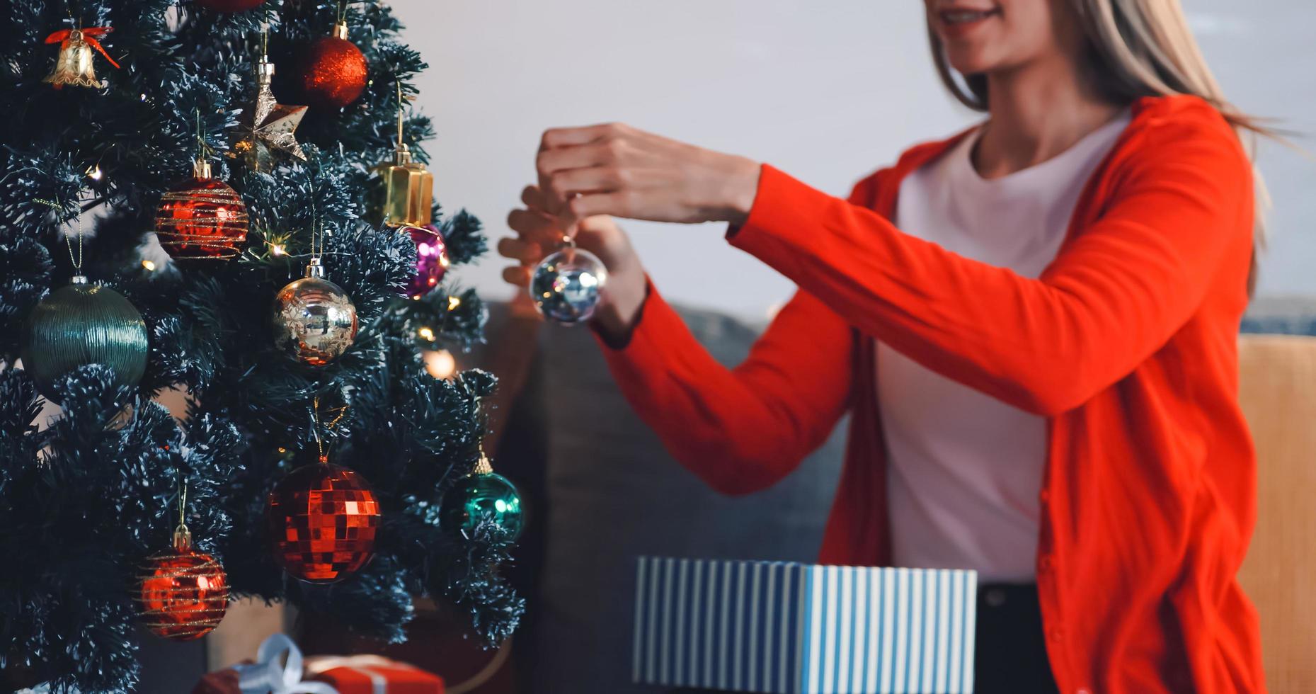 uma linda mulher está decorando um pinheiro para uma festa de natal em casa. foto