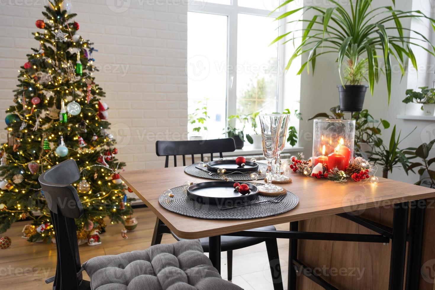 mesa festiva posta na sala de estar para o natal e ano novo em estilo loft. árvore de natal, pratos pretos e garfos, guardanapos tecidos, utensílios de mesa da moda, interior aconchegante da casa foto