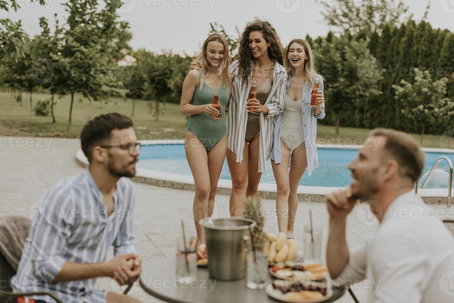 grupo de jovens torcendo com bebidas e comendo frutas à beira da piscina no jardim foto