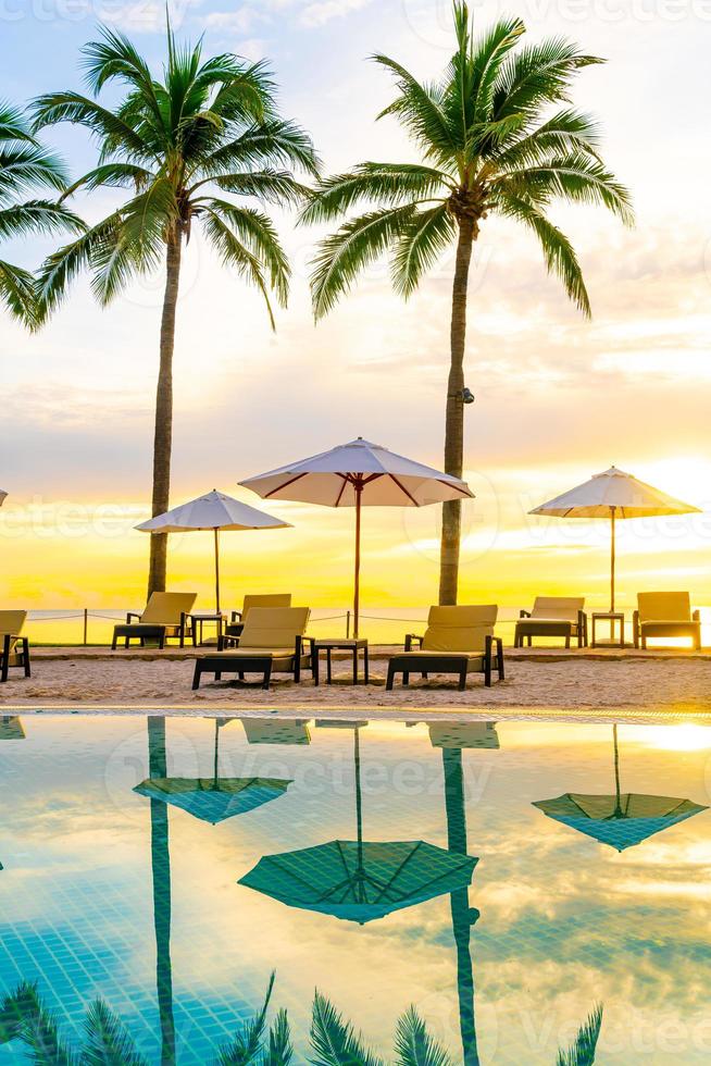 guarda-chuva e cadeira ao redor da piscina em hotel resort com nascer do sol pela manhã foto