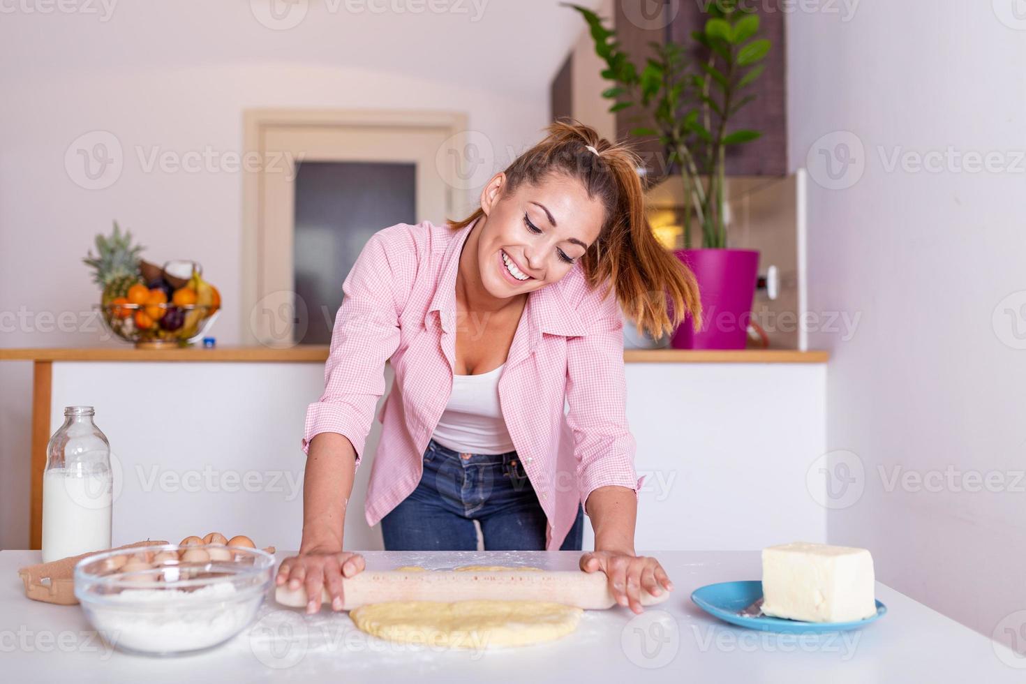 cozinha prepara massa de farinha feliz atraente jovem mulher dona de casa padeiro segurando o pino rolando massa na mesa da cozinha assando conceito de pastelaria cozinhando bolo biscoito fazendo padaria em casa foto