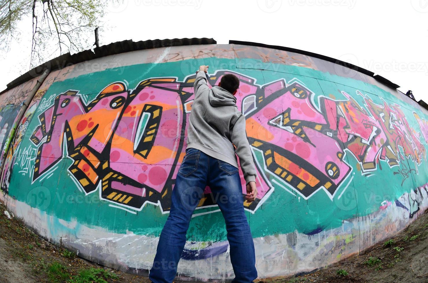 um jovem com um capuz cinza pinta graffiti em rosa e verde c foto