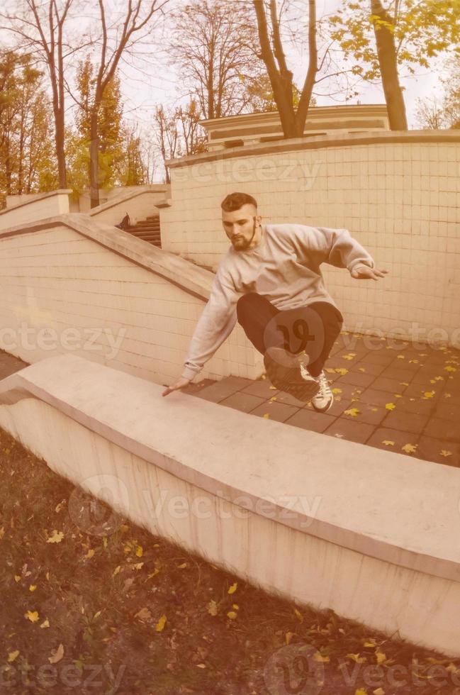 um jovem dá um salto pelo parapeito de concreto. o atleta pratica parkour, treinando em condições de rua. o conceito de subculturas esportivas entre os jovens foto