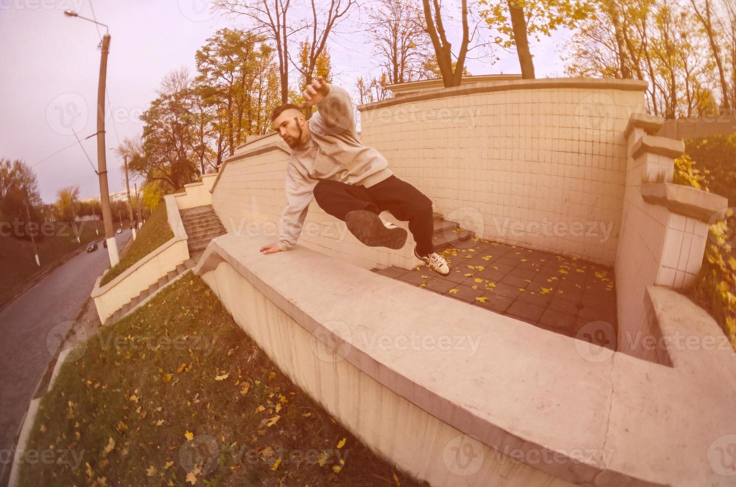 um jovem dá um salto pelo parapeito de concreto. o atleta pratica parkour, treinando em condições de rua. o conceito de subculturas esportivas entre os jovens foto