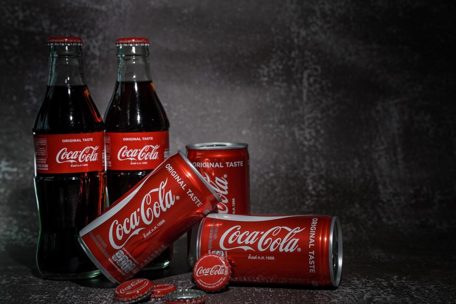 ayutthaya, tailândia-25 de junho de 2020- clássico da coca-cola em uma garrafa de vidro e lata em fundo de cimento em tons escuros. coca cola, o coque é o refrigerante carbonatado mais popular vendido em todo o mundo foto