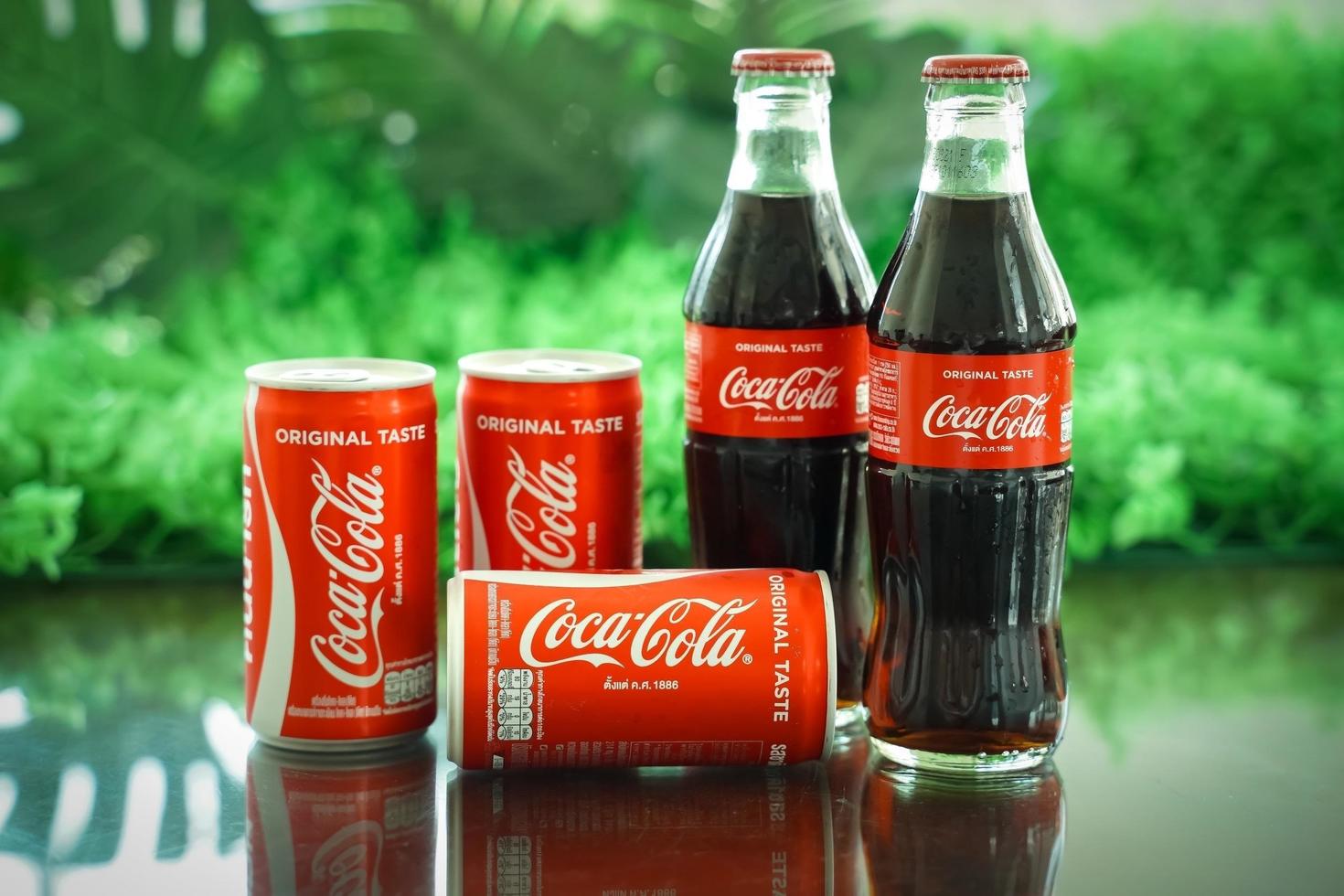 ayutthaya, tailândia-25 de junho de 2020- clássico da coca-cola em uma garrafa de vidro e lata em fundo de cimento em tons escuros. coca cola, o coque é o refrigerante carbonatado mais popular vendido em todo o mundo foto