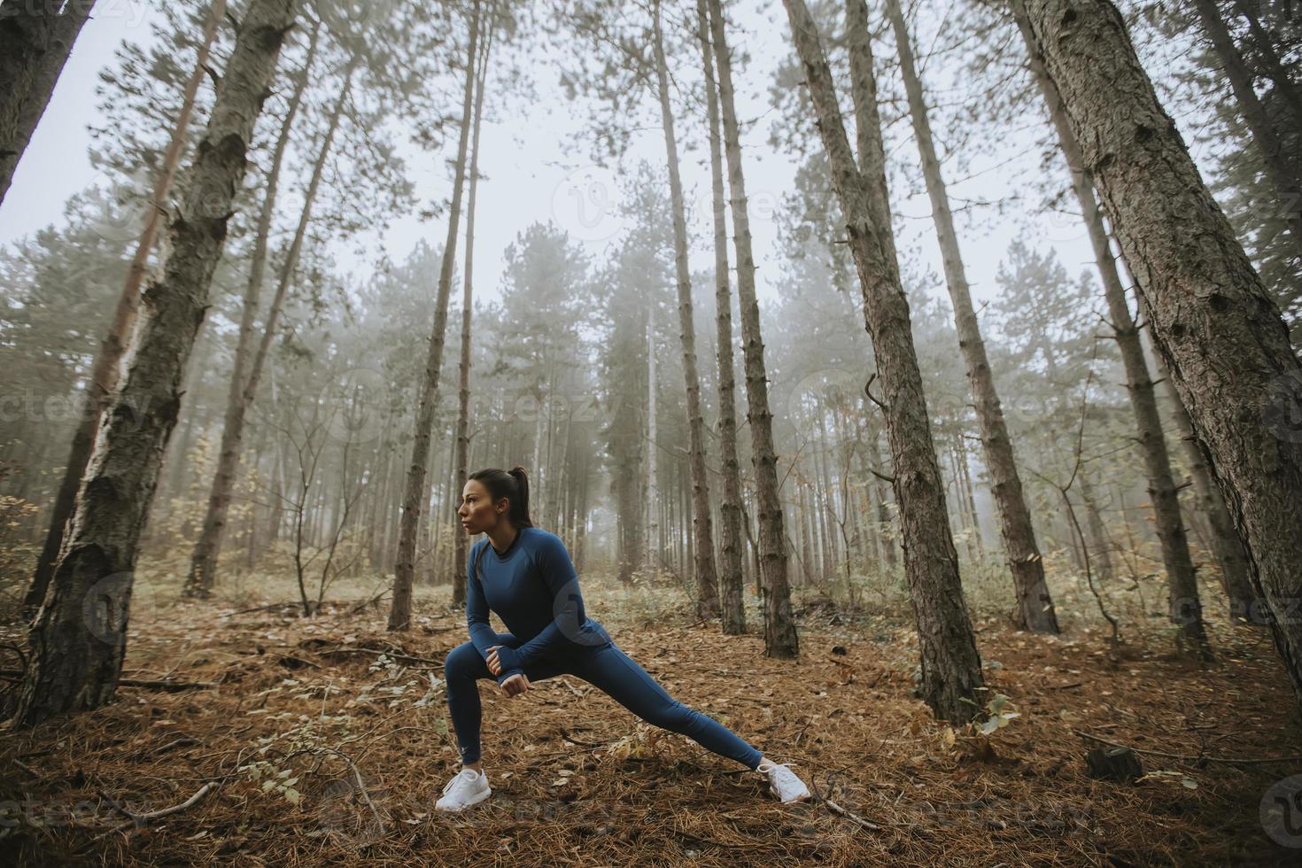 jovem com fato de treino azul alongamento antes do treino na floresta de outono foto