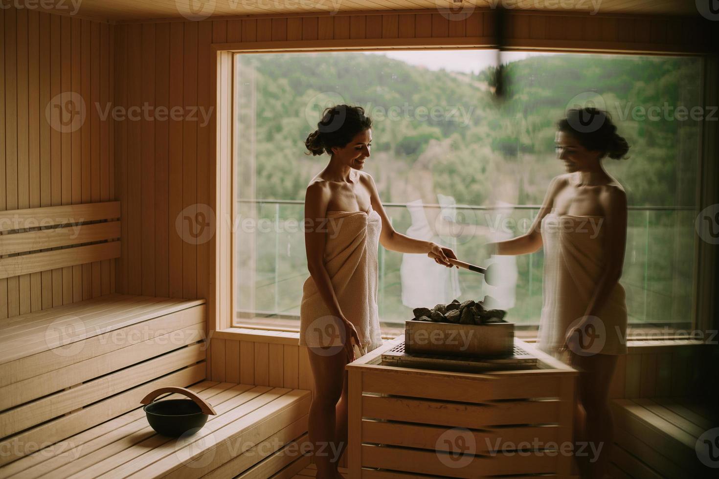jovem mulher despejando água em pedra quente na sauna foto