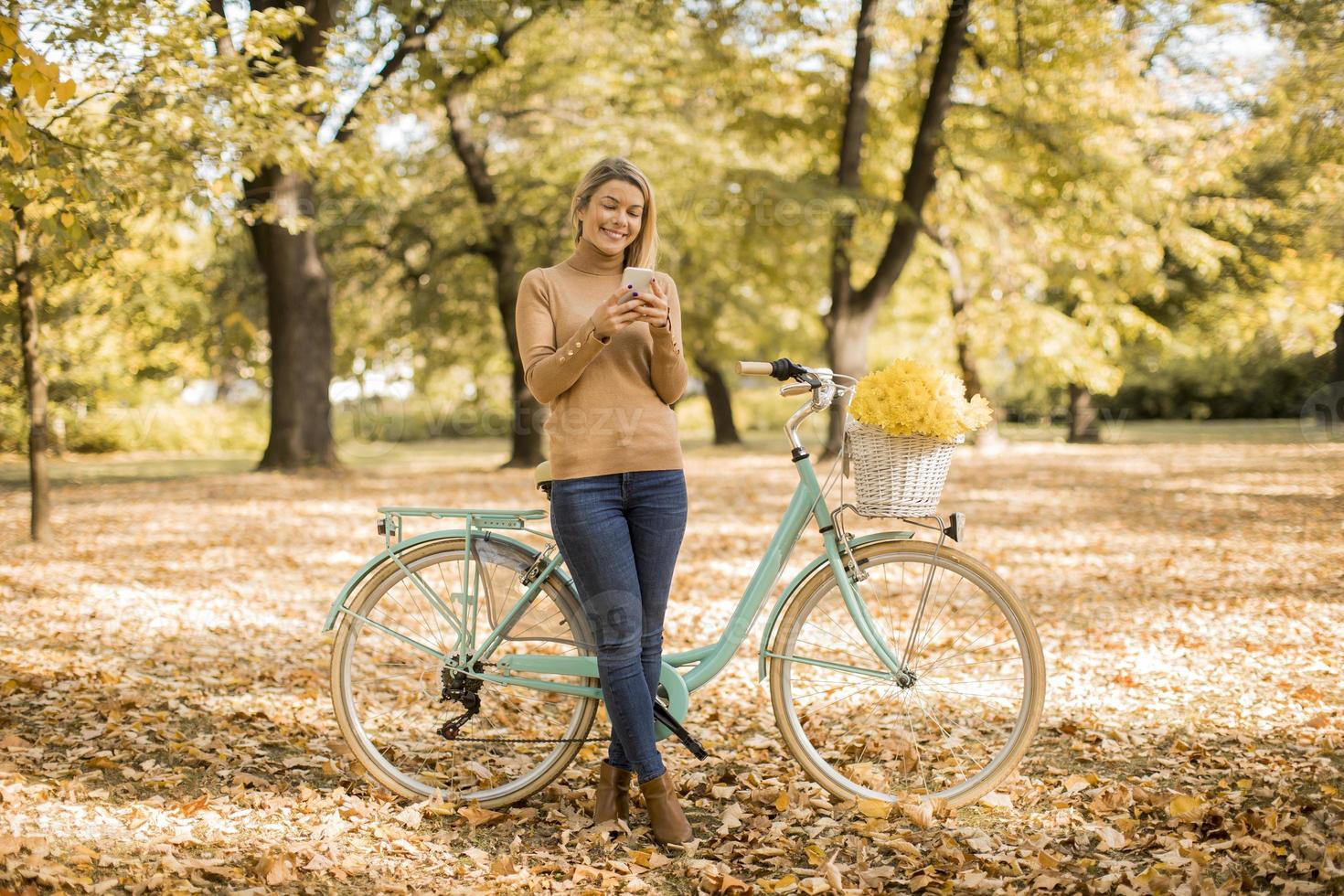 jovem mulher com bicicleta usando smartphone no parque outono foto