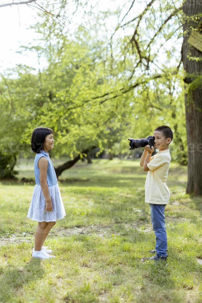 garotinho asiático agindo como um fotógrafo profissional enquanto tira fotos de sua irmãzinha