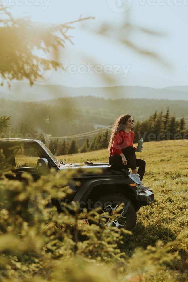 jovem relaxante em um capô de veículo de terreno na zona rural foto