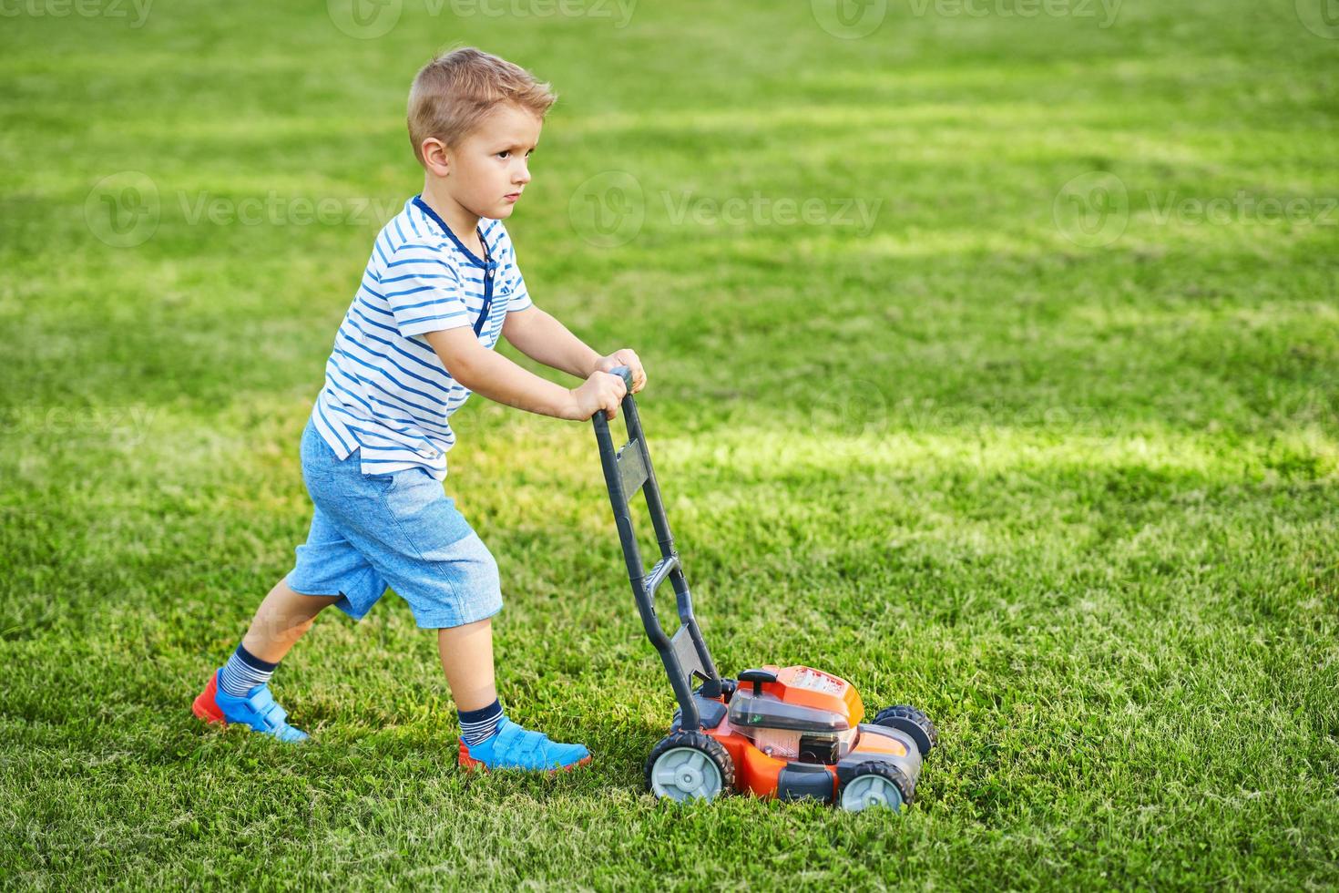 menino feliz de 3 anos se divertindo cortando grama foto