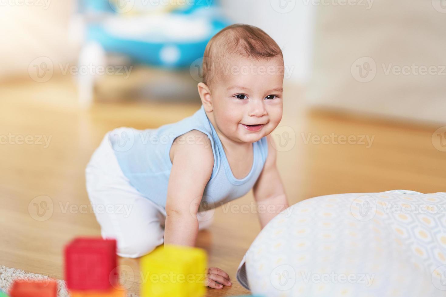 lindo menino sorridente rastejando no chão na sala de estar foto