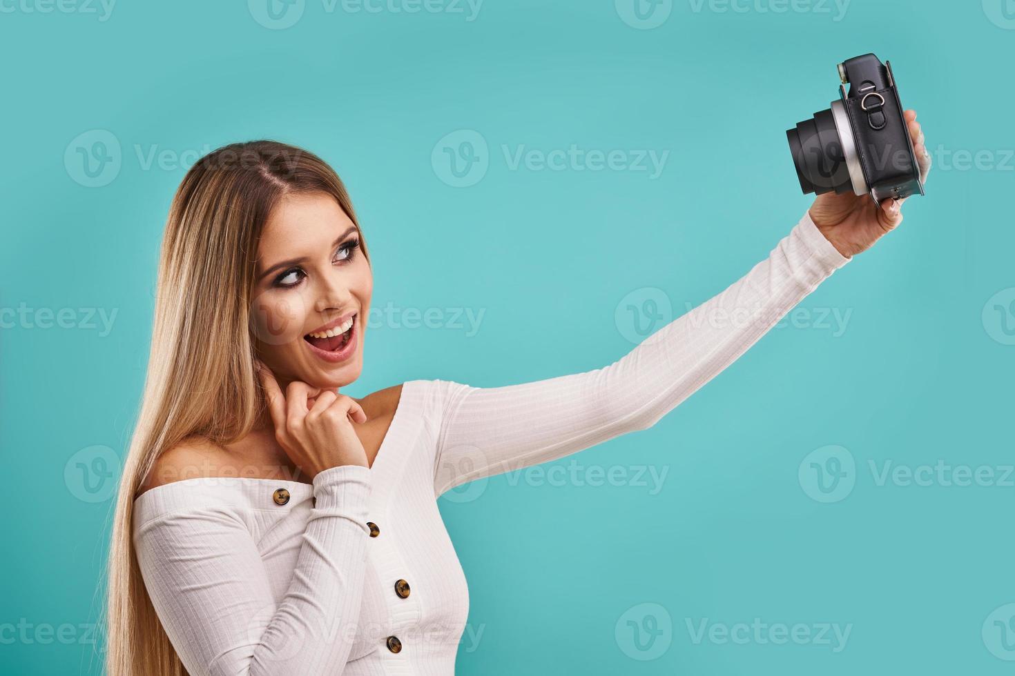 linda mulher adulta posando sobre fundo azul tirando fotos instantâneas