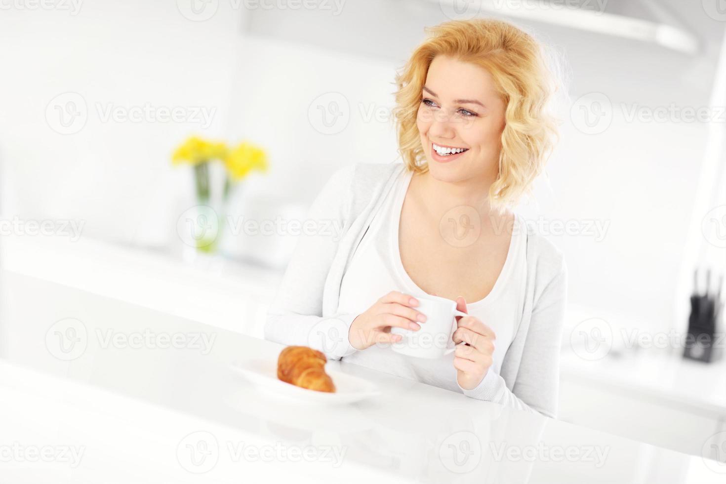 jovem mulher tomando café na cozinha foto