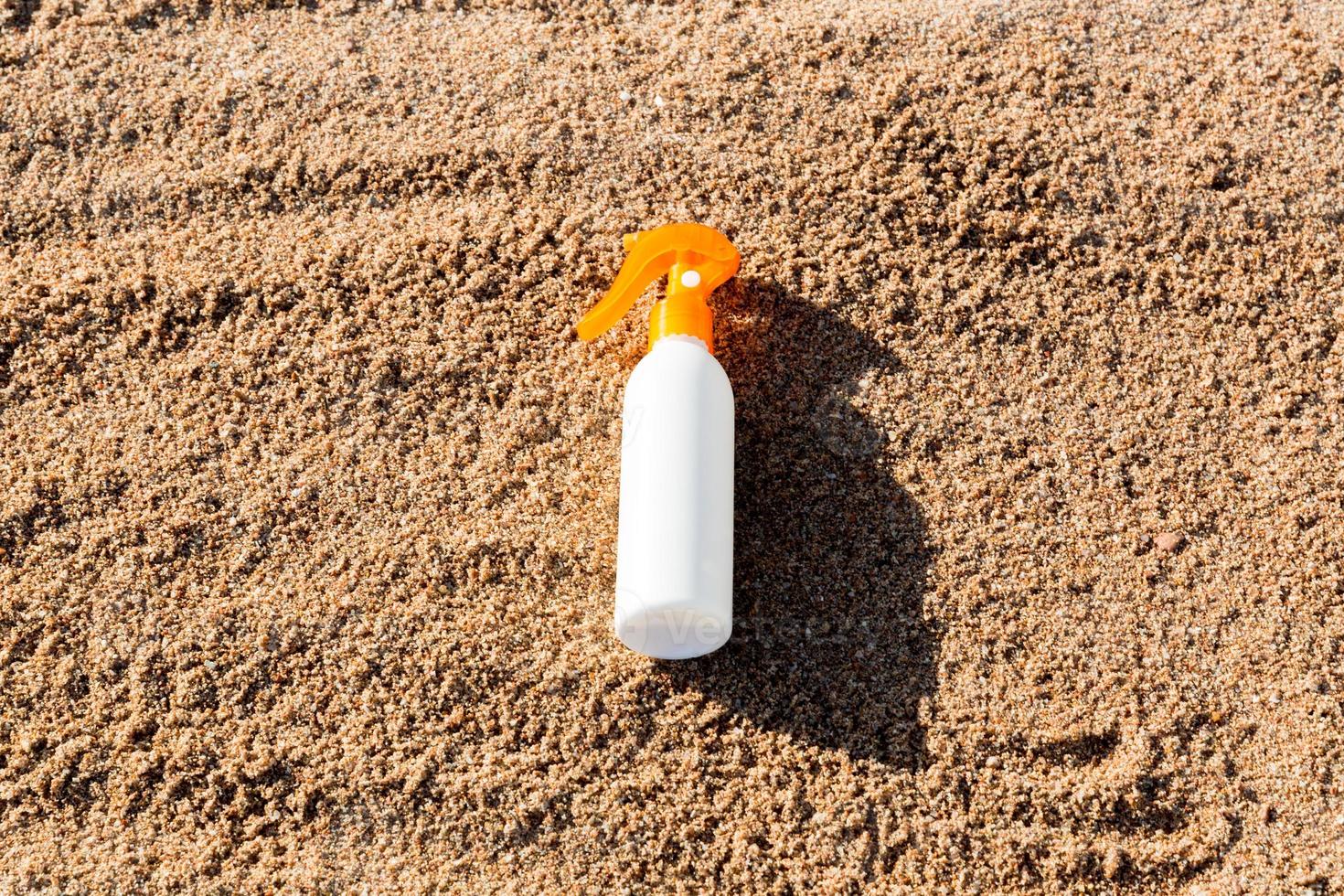 garrafa branca de loção bronzeadora na areia com espaço de cópia. protetor solar spf creme na praia do mar no conceito de férias de verão foto
