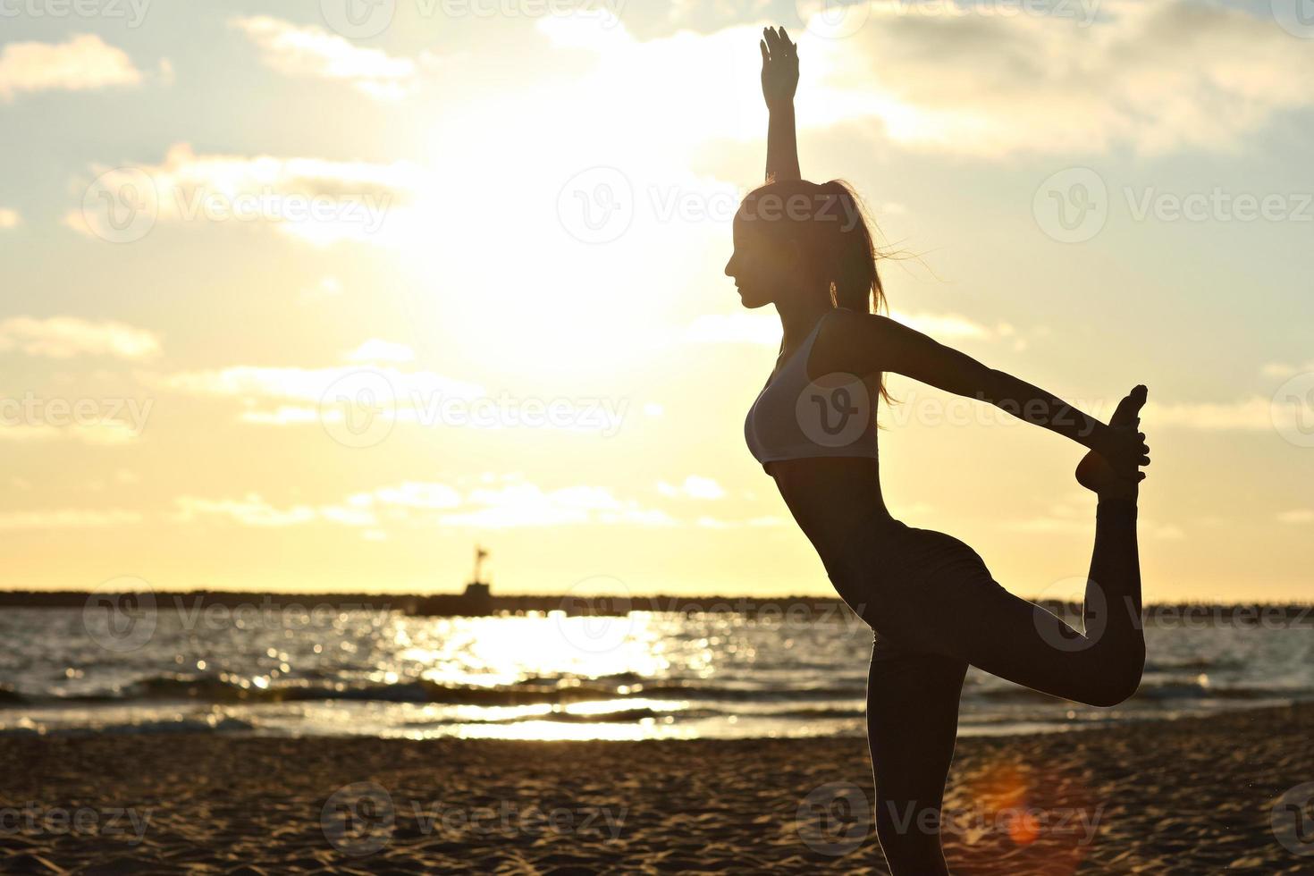 silhueta jovem praticando ioga na praia ao pôr do sol foto