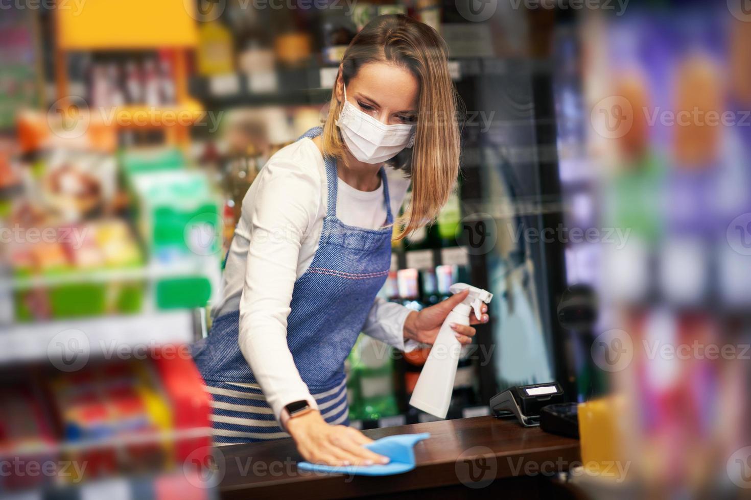 assistente de loja desinfetando superfícies em mercearia foto