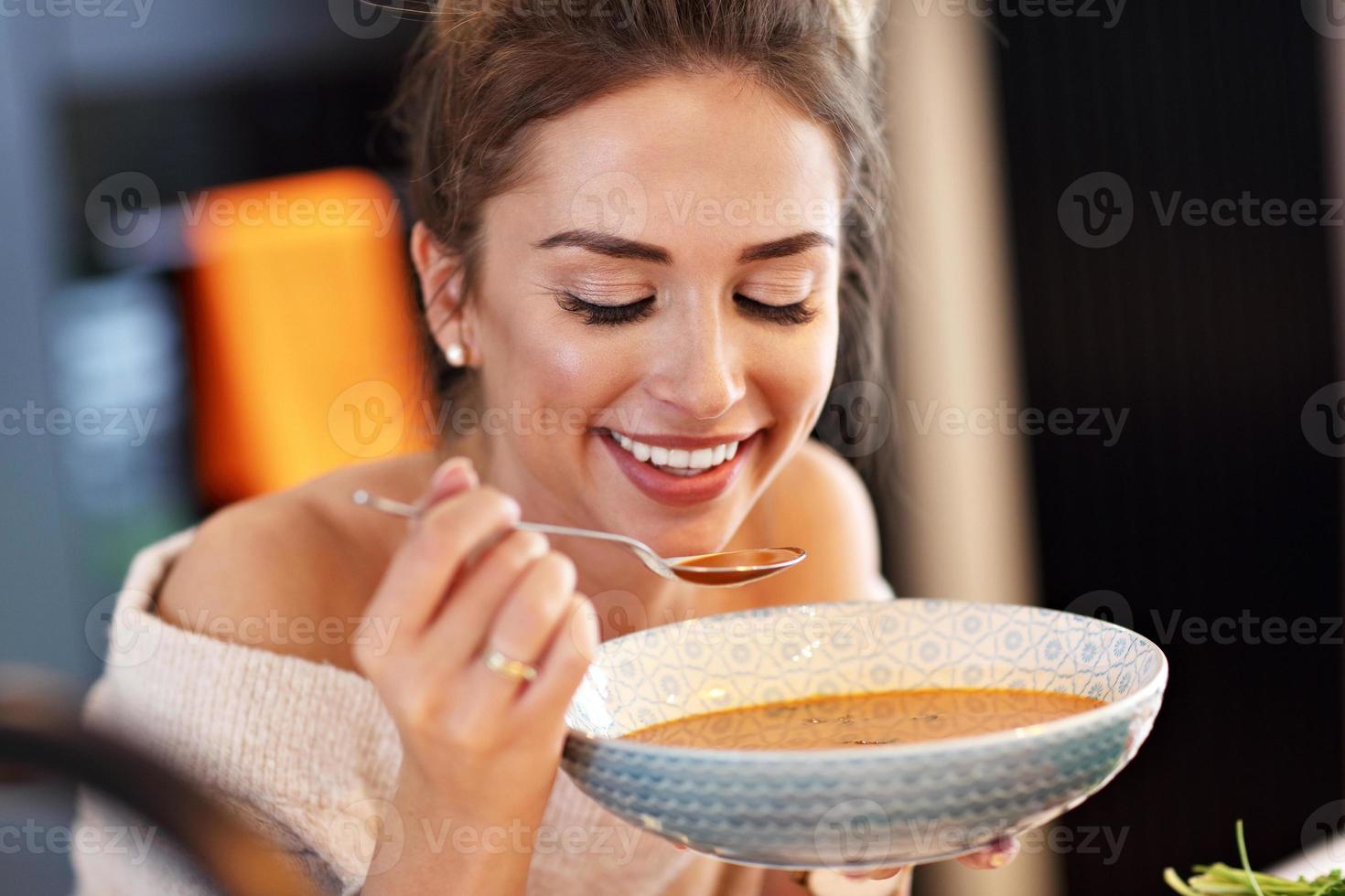 mulher adulta comendo sopa de abóbora na cozinha foto