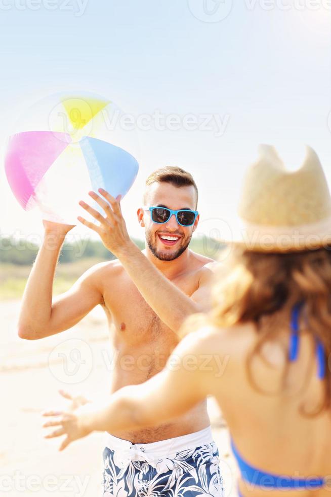 jovem casal brincando com uma bola na praia foto