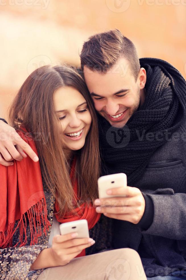 jovem casal sentado em um banco e usando smartphones foto