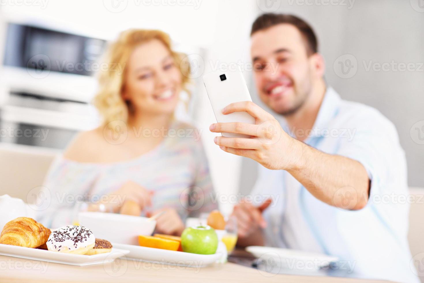 casal feliz tomando café da manhã e tirando selfie foto