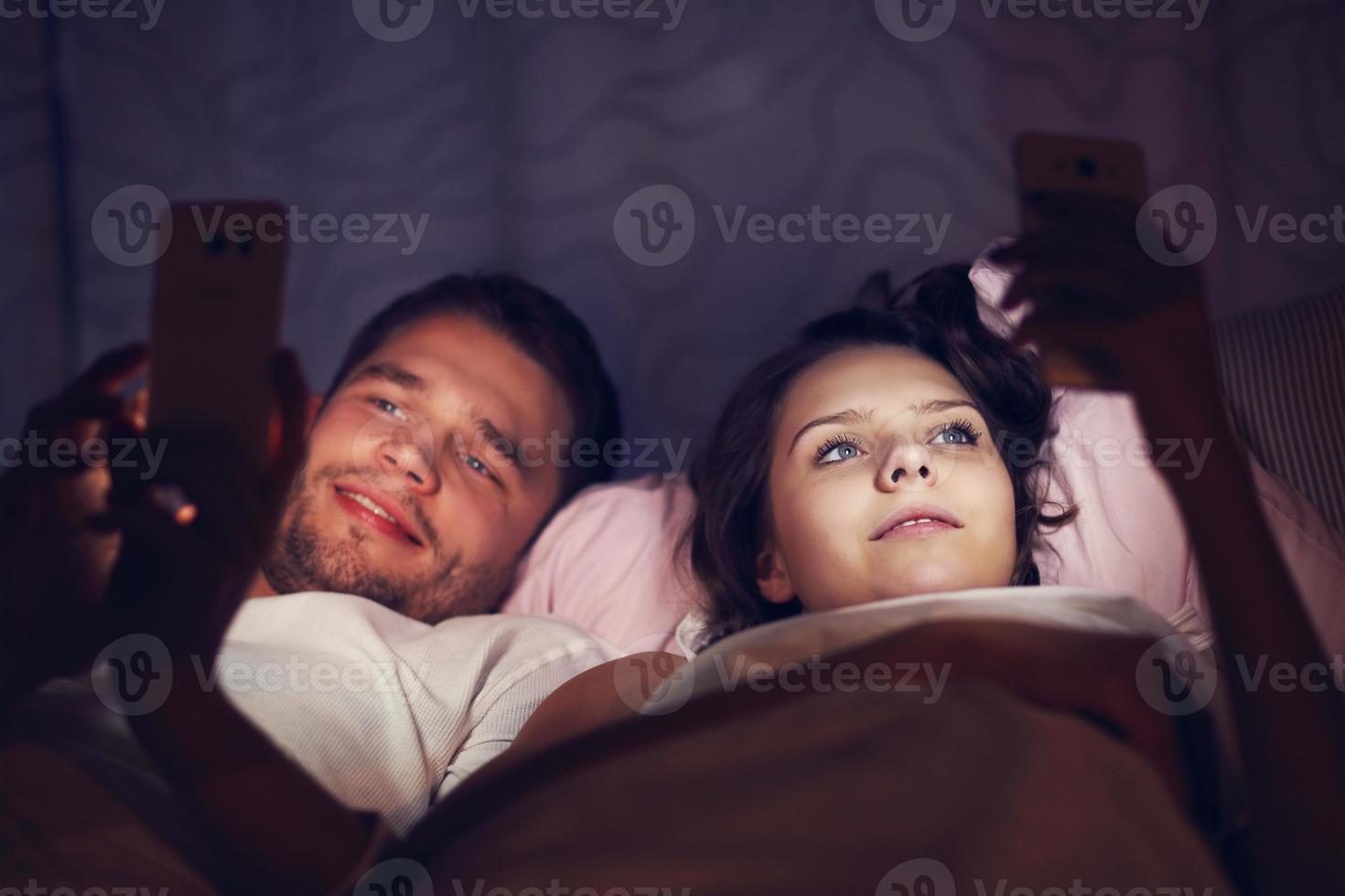 jovem casal usando smartphones na cama à noite foto