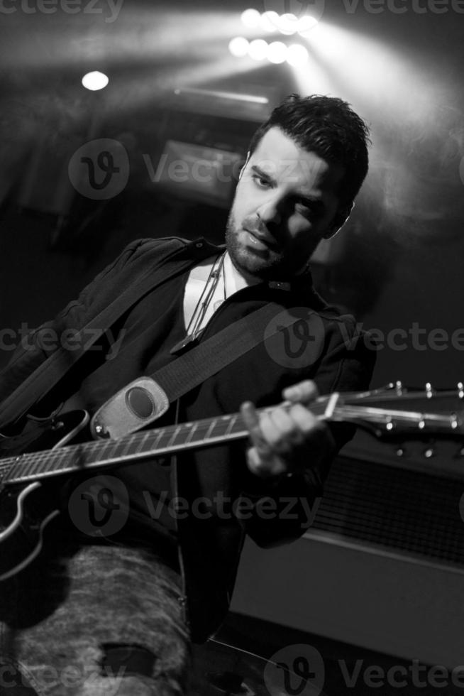 foto de retrato preto e branco de um modo masculino bonito tocando guitarra no palco. artista de guitarra no palco