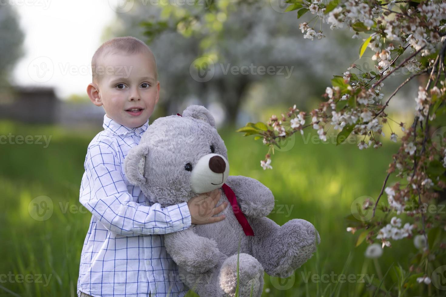 uma criança feliz em um jardim florido segura um urso de brinquedo. foto