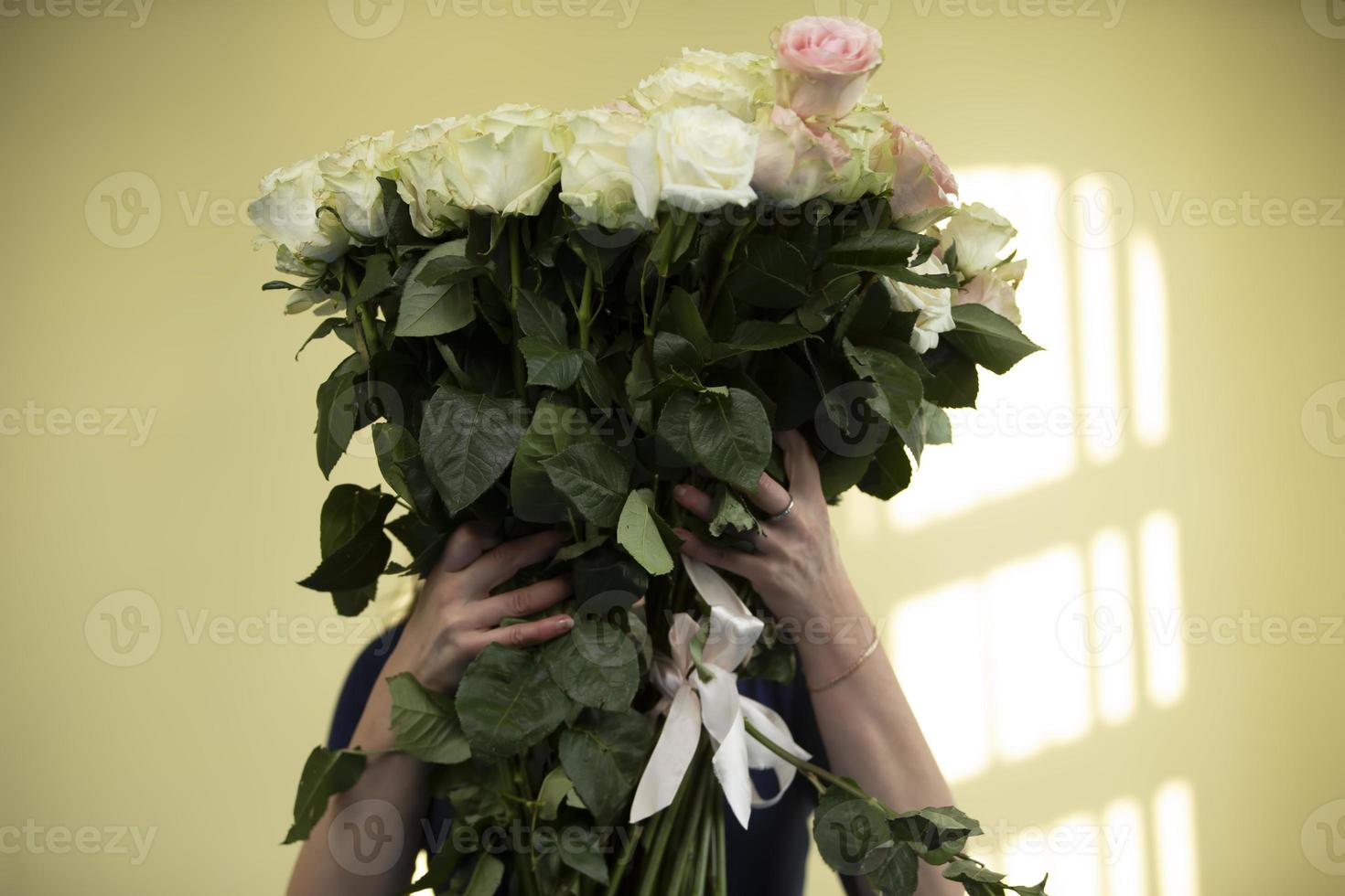 mulher segurando um enorme buquê de flores rosas brancas cobrindo o rosto foto