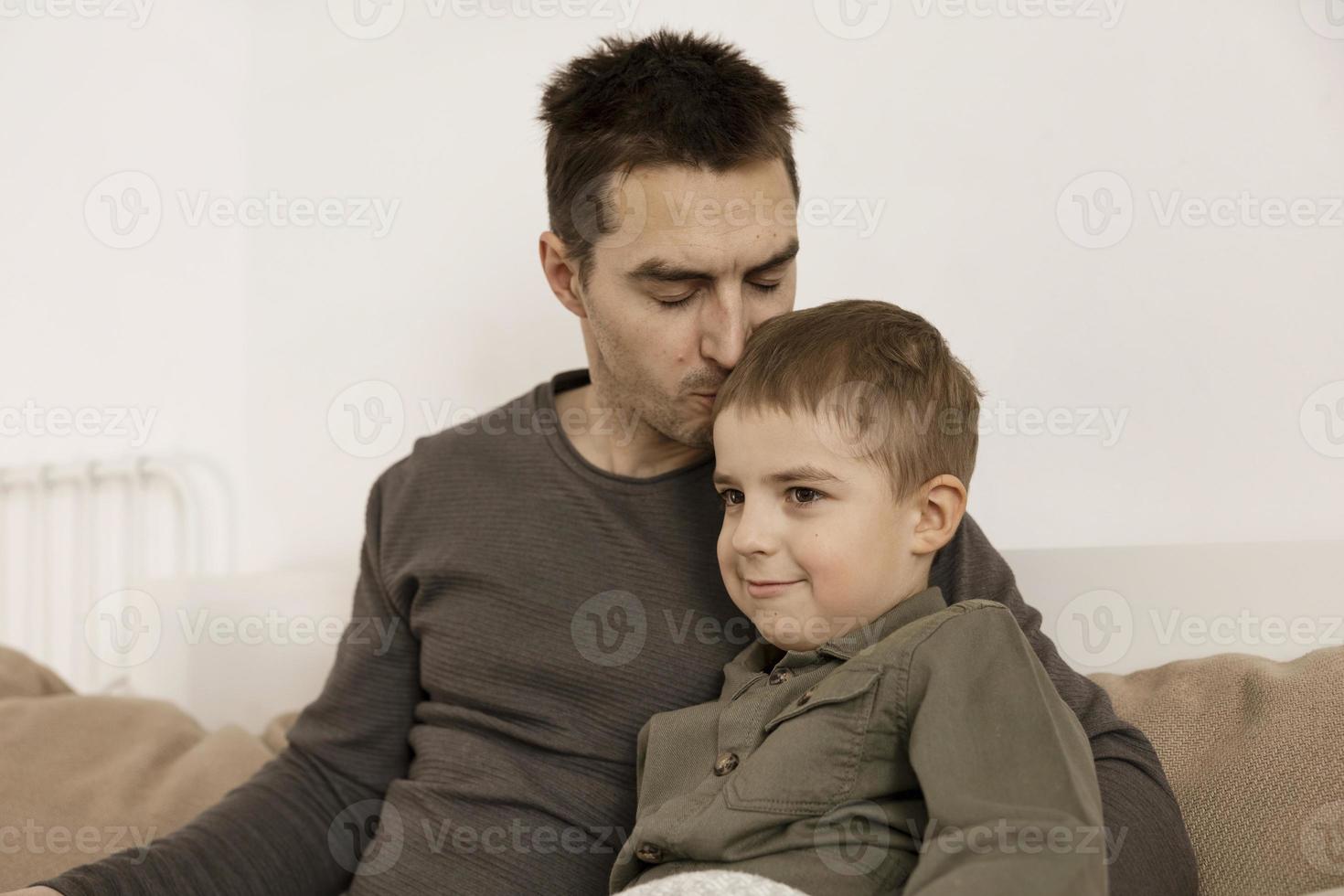 pai beijando seu filho. pai ama seu filho. jovem atraente e criança caucasiana se divertem juntos. interior e roupas em cores naturais da terra. ambiente aconchegante. foto