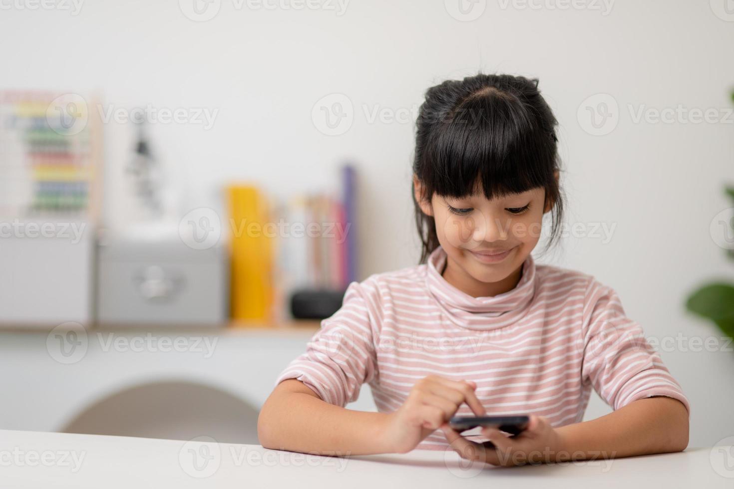 menina bonitinha usa smartphone enquanto está sentado no sofá da sala de estar. criança navegando na internet no celular, navega pela internet e assiste desenhos animados online em casa foto