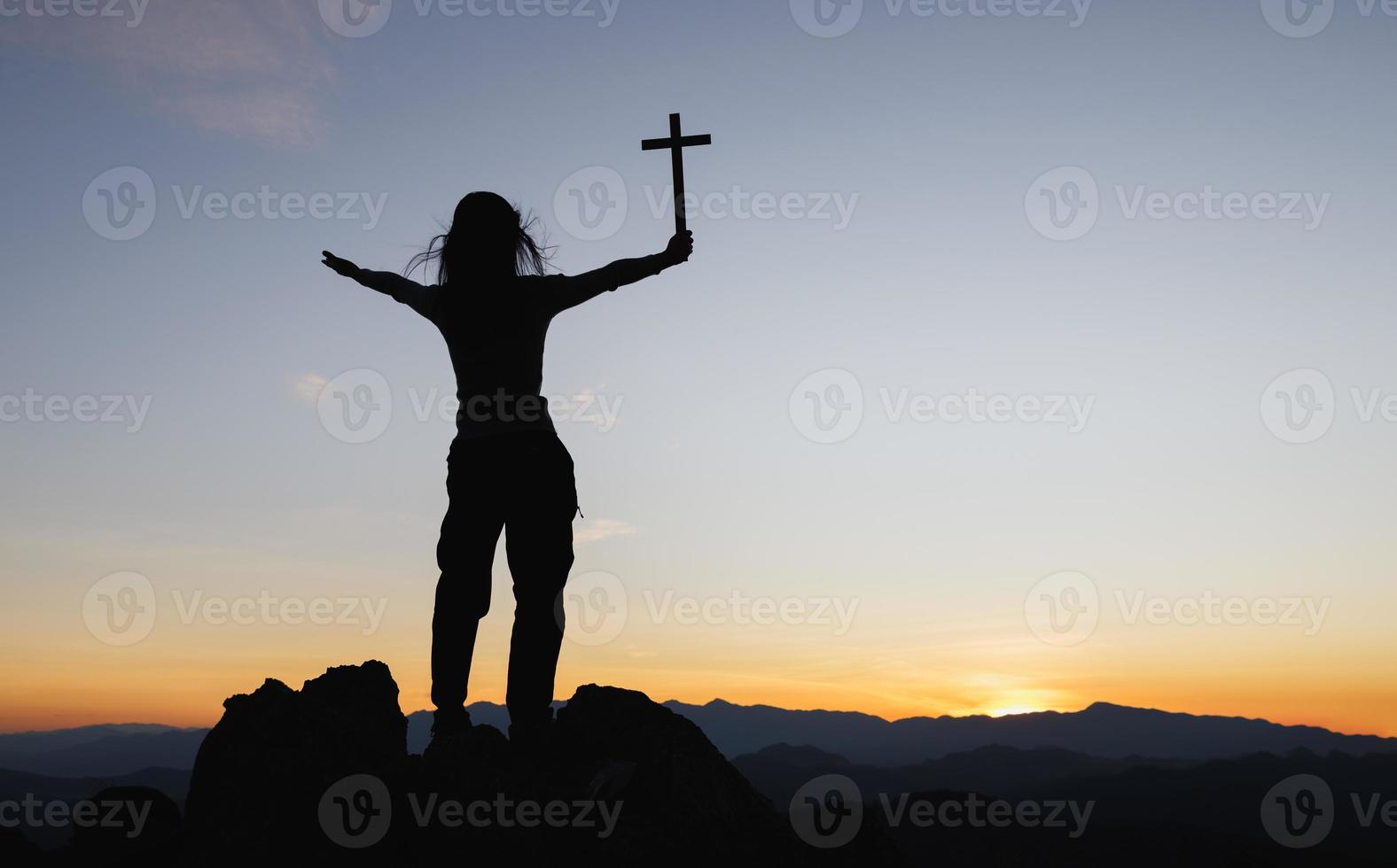 silhueta de jovem cristã rezando com uma cruz ao nascer do sol, fundo do conceito de religião cristã. foto