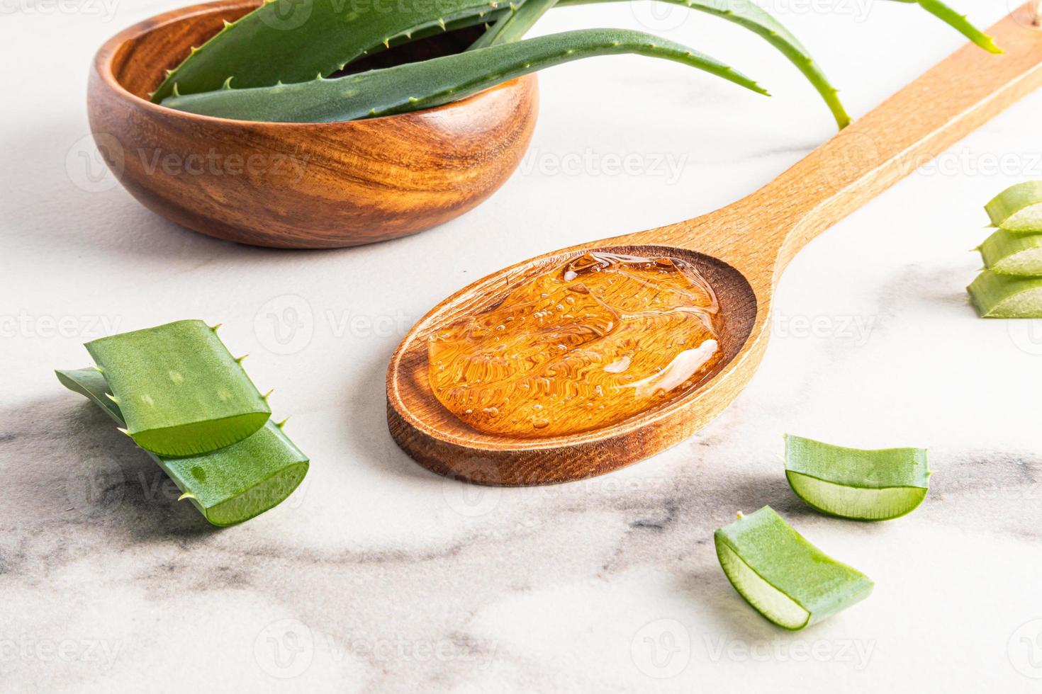 Extrair gel orgânico de aloe vera em uma colher de pau em um fundo branco de mármore. as folhas da planta na tigela. autocuidado cosmético. foto