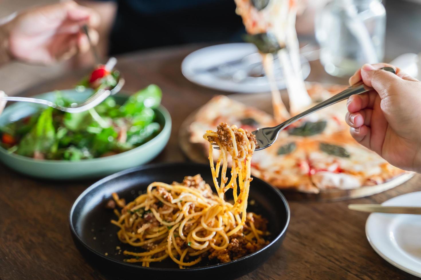 família ou amigos comendo comida juntos. pessoas comendo macarrão de comida italiana, pizza, salada na mesa. foto