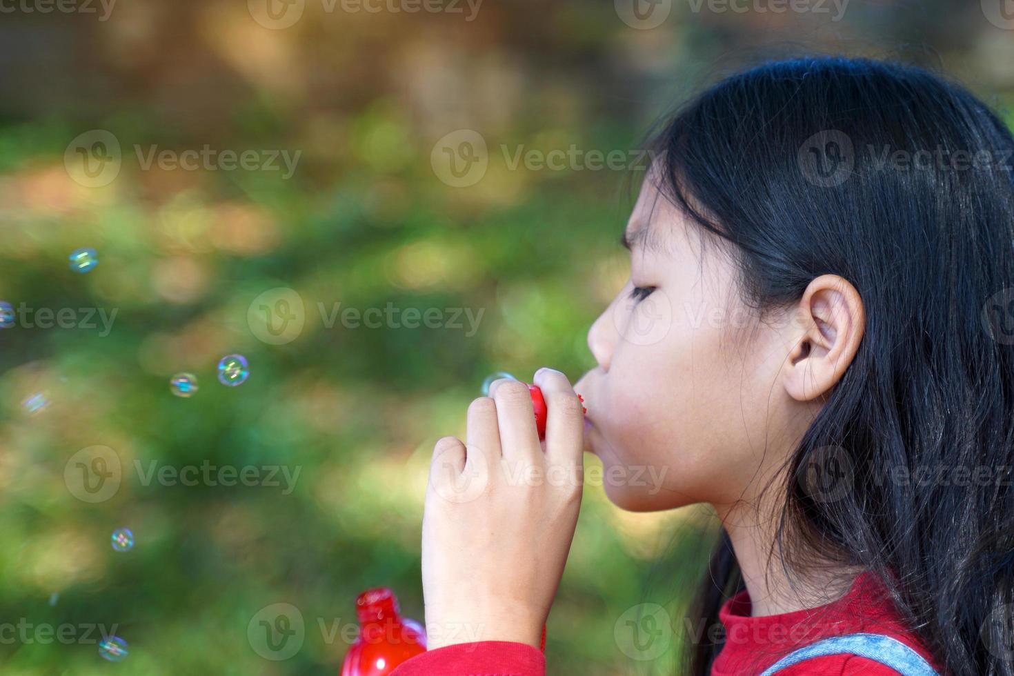 menina asiática soprando bolhas de sabão brincando ao ar livre no parque. jogo de conceito, brinquedos, atividades de lazer infantil. foco suave e seletivo. foto